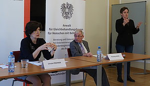 Ursula Frohner, Hansjörg Hofer und Barbara Gerstbach als Gebärdendolmetscherin vor einem Rollup des Behindertenanwalts